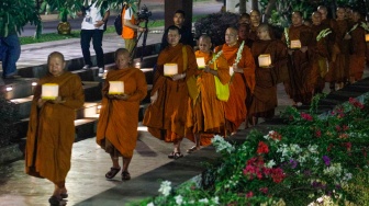 Para Bhikkhu berjalan sambil membawa lentera saat prosesi Walking Meditation di Taman Mini Indonesia Indah, Jakarta, Selasa (14/5/2024). [Suara.com/Alfian Winanto]