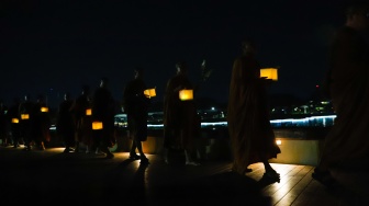 Para Bhikkhu berjalan sambil membawa lentera saat prosesi Walking Meditation di Taman Mini Indonesia Indah, Jakarta, Selasa (14/5/2024). [Suara.com/Alfian Winanto]