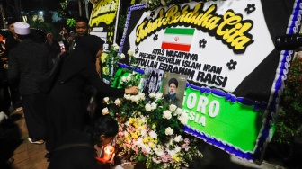 Warga meletakan bunga di tengah karangan bunga yang terpajang di depan Kantor Kedutaan Besar Iran, Jakarta, Senin (20/5/2024). [Suara.com/Alfian Winanto]