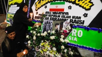 Warga meletakan bunga di tengah karangan bunga yang terpajang di depan Kantor Kedutaan Besar Iran, Jakarta, Senin (20/5/2024). [Suara.com/Alfian Winanto]