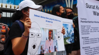 Massa membawa poster saat menggelar aksi di depan gedung Kementerian Komunikasi dan Informatika (Kemenkominfo) di Jakarta, Rabu (10/7/2024). [Suara.com/Alfian Winanto]