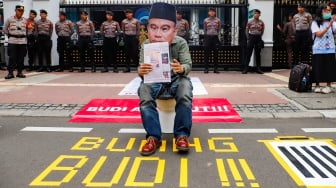 Seorang pengunjuk rasa duduk diatas closet memakai topeng wajah Menkominfo Budi Arie Setiadi saat menggelar aksi di depan gedung Kementerian Komunikasi dan Informatika (Kemenkominfo) di Jakarta, Rabu (10/7/2024). [Suara.com/Alfian Winanto]