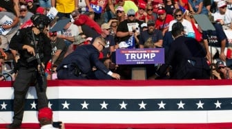 Kandidat Partai Republik dan mantan Presiden AS Donald Trump berlindung dan dikelilingi oleh agen Secret Service  di atas panggung saat insiden penembakan pada acara kampanye di Butler Farm Show Inc. di Butler, Pennsylvania, Sabtu (13/7/2024). [Rebecca DROKE/AFP]