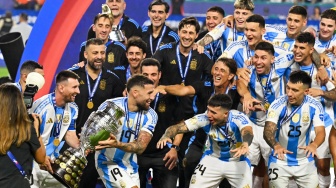 Penyerang Argentina Lionel Messi dan bek Argentina Nicolas Otamendi berjalan dengan trofi saat ia merayakan kemenangan pertandingan sepak bola final Copa America 2024 antara Argentina dan Kolombia di Stadion Hard Rock, di Miami, Florida, Minggu (14/7/2024). [Chandan Khanna / AFP]