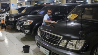 Penjual membersihkan mobil bekas yang dijual di bursa mobil bekas Blok M, Jakarta, Jumat (19/7/2024). [Suara.com/Alfian Winanto]