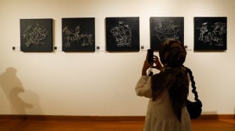 Pengunjung mengamati lukisan yang ditampilkan saat berkunjung ke pameran "Patung dan Aktivisme: Dolorosa Sinaga dan Budi Santoso" di Galeri Nasional Indonesia, Jakarta, Minggu (28/7/2024). [Suara.com/Alfian Winanto]