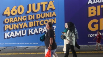 Warga melintas dengan latar iklan bitcoin di Terowongan Kendal, Jakarta, Selasa (24/9/2024). [Suara.com/Alfian Winanto]