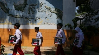 Pelajar membawa bingkai foto presiden Prabowo Subianto dan wakil presiden Gibran Rakabuming Raka di SDN Pondok Labu 14 Pagi, Jakarta, Selasa (22/10/2024). [Suara.com/Alfian Winanto]