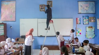 Petugas dibantu pelajar memasang bingkai foto presiden Prabowo Subianto dan wakil presiden Gibran Rakabuming Raka di SDN Pondok Labu 14 Pagi, Jakarta, Selasa (22/10/2024). [Suara.com/Alfian Winanto]