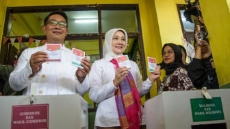 Calon gubernur (Cagub) DKI Jakarta nomor urut 1 Ridwan Kamil (kiri) bersama istri sekaligus Anggota Komisi VIII DPR RI Atalia Praratya (kedua kiri) menunjukkan surat suara sebelum dimasukkan ke kotak suara saat menggunakan hak pilihnya pada pilkada serentak 2024 di Tempàat Pemungutan Suara (TPS) 23 Kelurahan Ciumbuleuit, Bandung, Jawa Barat, Rabu (27/11/2024). [ANTARA FOTO/Novrian Arbi]