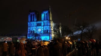 Kerumunan orang berdiri saat lampu-lampu dinyalakan dalam upacara pembukaan kembali Katedral Notre Dame di Paris, Prancis, Minggu (8/12/2024). [Dimitar DILKOFF / AFP]