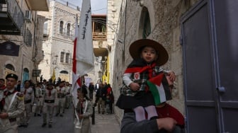 Pramuka Palestina mengangkat spanduk saat mereka mengambil bagian dalam prosesi Natal tahunan menuju Gereja Kelahiran di kota Betlehem di Tepi Barat Palestina yang diduduki Israel pada Selasa (24/12/2024). [HAZEM BADER / AFP]