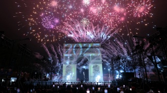 Kembang api menerangi langit di sekitar Arc de Triomphe di Avenue des Champs-Elysees di Paris, Prancis, Rabu (1/1/2025). [Thomas SAMSON / AFP]