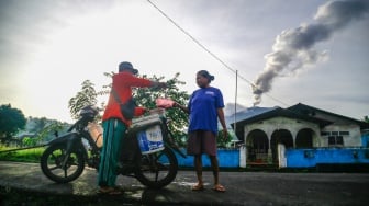 Warga berbelanja ikan dengan latar belakang Gunung Ibu mengeluarkan asap vulkanik dari kawah gunung terlihat di Desa Duono Kabupaten Halmahera Barat, Maluku Utara, Rabu(15/1/2024). [ANTARA FOTO/Andri Saputra/foc]