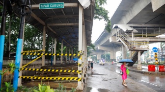 Warga melintas di samping Halte dan Jembatan Penyeberangan Orang (JPO) Tipar Cakung yang rusak di Jakarta, Sabtu (26/4/2025). [Suara.com/Alfian Winanto]
