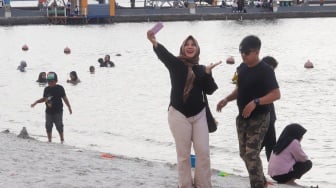 Pengunjung berwisata di Pantai Lagoon, Taman Impian Jaya Ancol, Jakarta, Selasa (13/5/2025). [Suara.com/Alfian Winanto]