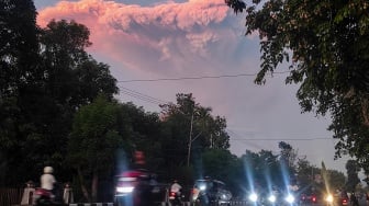 Pengendara motor melintas berlatar belakang awan panas erupsi Gunung Lewotobi Laki-laki di Maumere, Kabupaten Sikka, Nusa Tenggara Timur, Selasa (17/6/2025). [ANTARA FOTO/Arnoldine Shanon/sgd/foc]