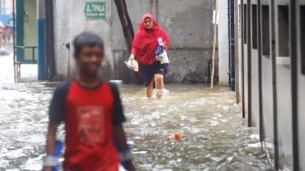 Warga beraktivitas di tengah banjir yang melanda di Jalan Tipala, Makasar, Jakarta Timur, Senin (7/7/2025). [Suara.com/Alfian Winanto]