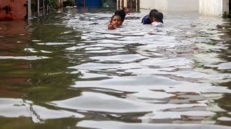 Warga beraktivitas di tengah banjir yang melanda di Jalan Tipala, Makasar, Jakarta Timur, Senin (7/7/2025). [Suara.com/Alfian Winanto]