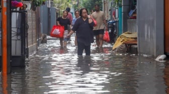 Warga beraktivitas di tengah banjir yang melanda di Jalan Tipala, Makasar, Jakarta Timur, Senin (7/7/2025). [Suara.com/Alfian Winanto]