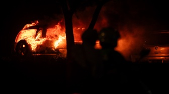 Pengendara motor melintas disamping mobil yang terbakar saat aksi unjuk rasa di depan Markas Komando (Mako) Brimob Polda Mtero Jaya, Kwitang, Jakarta, Jumat (29/8/2025)malam. [ANTARA FOTO/Bayu Pratama S/wpa]