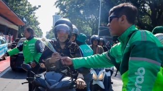 Pengemudi ojek online (ojol) membagikan bunga ke pengguna jalan saat aksi damai di Jalan Merdeka Selatan, Jakarta, Selasa (2/9/2025). [Suara.com/Alfian Winanto]