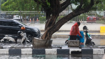 Pengendara berteduh dan memakai jas hujan saat hujan di Kawasan Slipi, Jakarta, Senin (29/9/2025). [Suara.com/Alfian Winanto]