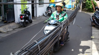 Warga beraktivitas di dekat jaringan kabel utilitas yang menjuntai di kawasan Setiabudi, Jakarta, Rabu (12/11/2025). [Suara.com/Alfian Winanto]