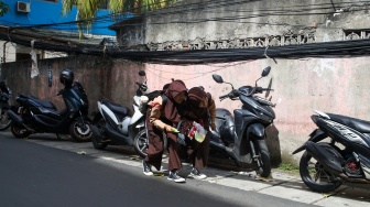 Warga beraktivitas di dekat jaringan kabel utilitas yang menjuntai di kawasan Setiabudi, Jakarta, Rabu (12/11/2025). [Suara.com/Alfian Winanto]