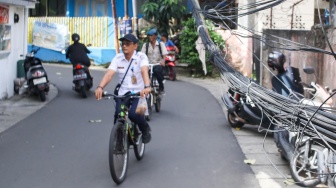 Warga beraktivitas di dekat jaringan kabel utilitas yang menjuntai di kawasan Setiabudi, Jakarta, Rabu (12/11/2025). [Suara.com/Alfian Winanto]