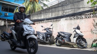 Warga beraktivitas di dekat jaringan kabel utilitas yang menjuntai di kawasan Setiabudi, Jakarta, Rabu (12/11/2025). [Suara.com/Alfian Winanto]