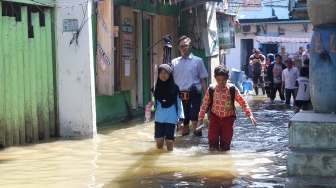 Pengguna jalan melintasi banjir rob di Muara Angke, Jakarta, Jumat (5/12/2025). [Suara.com/Alfian Winanto]