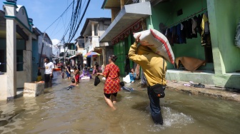 Pengguna jalan melintasi banjir rob di Muara Angke, Jakarta, Jumat (5/12/2025). [Suara.com/Alfian Winanto]