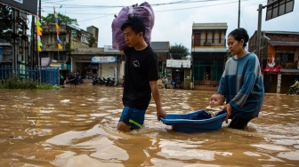 Warga membawa bayinya menggunakan ember saat melintasi banjir di Jalan Raya Dayeuhkolot, Kabupaten Bandung, Jawa Barat, Sabtu (6/12/2025). [ANTARA FOTO/Novrian Arbi/foc]