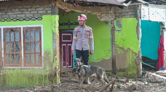 Pawang Unit K-9 Polri bersama anjing pelacak berdiri di depan rumah yang terdampak banjir bandang di Nagari Salareh Aia Timur, Palembayan, Agam, Sumatera Barat, Senin (8/12/2025). [ANTARA FOTO/Wahdi Septiawan/nz]