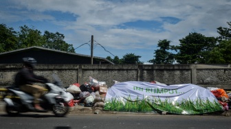 Pengendara motor melintas di samping tumpukan sampah yang ditutupi terpal di Ciater, Tangerang Selatan, Banten, Selasa (16/12/2025). [ANTARA FOTO/Putra M. Akbar/foc]
