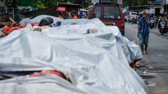Warga menutup hidungnya saat berjalan di samping tumpukan sampah yang ditutupi terpal di Serpong, Tangerang Selatan, Banten, Selasa (16/12/2025). [ANTARA FOTO/Putra M. Akbar/foc]