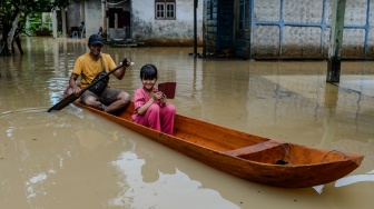 Seorang bapak bersama anaknya menggunakan perahu kayu menerobos banjir di Kampung Kajaroan, Cinangka, Kabupaten Serang, Banten, Kamis (18/12/2025). [ANTARA FOTO/Muhammad Bagus Khoirunas/YU]