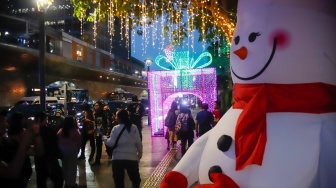Warga melihat instalasi pencahayaan pada Jakarta Light Festival 2025 di kawasan Bundaran HI, Jakarta, Selasa (23/12/2025). [Suara.com/Alfian Winanto]
