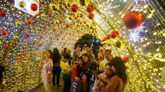 Warga melihat instalasi pencahayaan pada Jakarta Light Festival 2025 di kawasan Bundaran HI, Jakarta, Selasa (23/12/2025). [Suara.com/Alfian Winanto]
