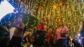 Warga melihat instalasi pencahayaan pada Jakarta Light Festival 2025 di kawasan Bundaran HI, Jakarta, Selasa (23/12/2025). [Suara.com/Alfian Winanto]

