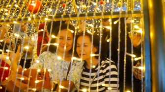 Warga berswafoto saat melihat instalasi pencahayaan pada Jakarta Light Festival 2025 di kawasan Bundaran HI, Jakarta, Selasa (23/12/2025). [Suara.com/Alfian Winanto]
