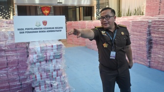 Petugas dari Kejaksaan Agung melintas di tengah tumpukan uang hasil penagihan denda administratif kehutanan dan penyelamatan keuangan negara dari hasil tindak pidana korupsi di kompleks Kejaksaan Agung, Jakarta, Rabu (24/12/2025). [ANTARA FOTO/Aditya Pradana Putra/sgd]