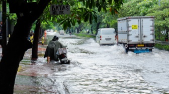Pengendara mendorong motornya melewati banjir yang menggenang di Jalan Danau Sunter Raya, Jakarta, Senin (12/1/2026). [Suara.com/Alfian Winanto]