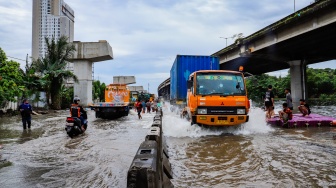 Kendaraan truk melewati banjir yang menggenang di Jalan RE Martadinata, Tanjung Priok, Jakarta, Senin (12/1/2026). [Suara.com/Alfian Winanto]