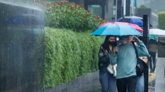 Sejumlah warga beraktivitas saat turun hujan di kawasan Bundaran HI, Jakarta, Selasa (13/1/2026). [Suara.com/Alfian Winanto]
