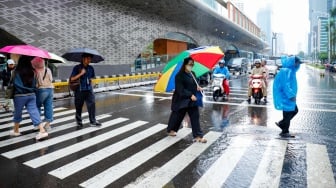 Sejumlah warga beraktivitas saat turun hujan di kawasan Bundaran HI, Jakarta, Selasa (13/1/2026). [Suara.com/Alfian Winanto]
