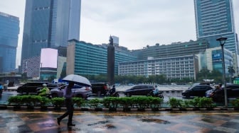 Sejumlah warga beraktivitas saat turun hujan di kawasan Bundaran HI, Jakarta, Selasa (13/1/2026). [Suara.com/Alfian Winanto]
