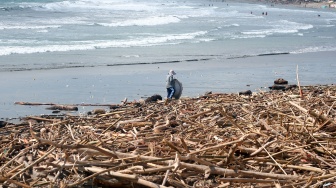 Seorang warga berdiri di atas tumpukan sampah kiriman di Pantai Kuta, Badung, Bali, Senin (19/1/2026). [ANTARA FOTO/Nyoman Hendra Wibowo/tom]