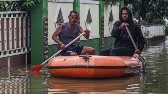 Dua warga menggunakan perahu untuk melintasi permukiman yang terendam banjir di Desa Karangligar, Telukjambe, Karawang, Jawa Barat, Kamis (22/1/2026). [ANTARA FOTO/Darryl Ramadhan/app/tom]